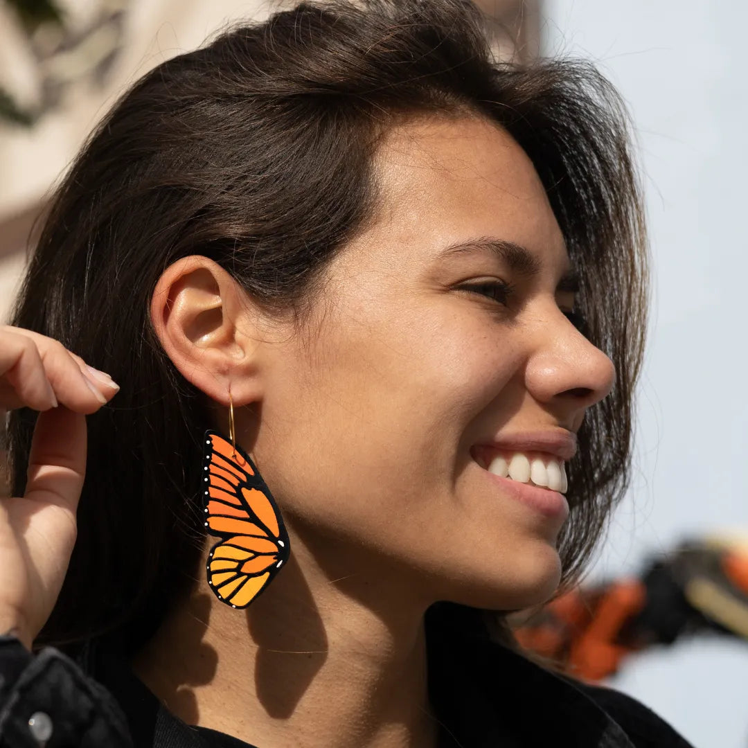 Close-up of woman smiling while wearing a hand-painted monarch butterfly wing hoop earring in bright sunlight.